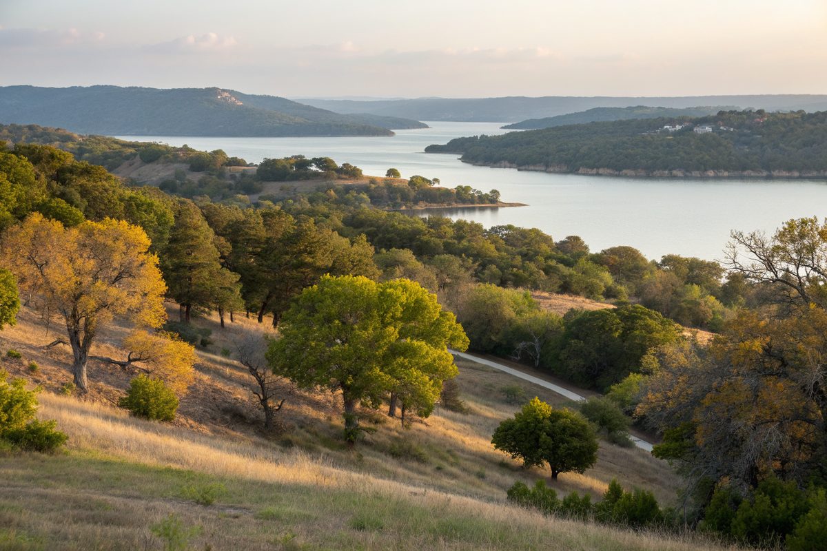 Wooded hills of cedar and oak above a lake shoreline in early light